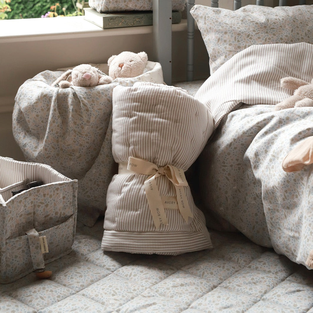 Baby items including a quilt, teddy bear, and storage bag on a textured surface.