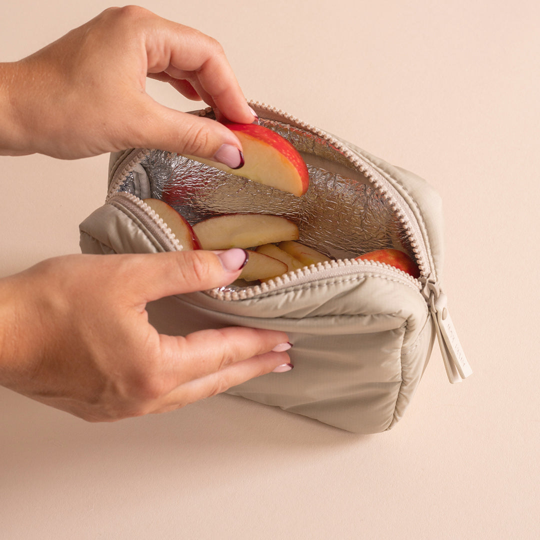 Hands opening a small beige insulated bag containing apples on a beige background