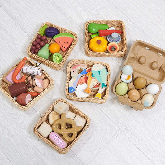 Set of colorful toy food items in wicker baskets on a light wooden surface