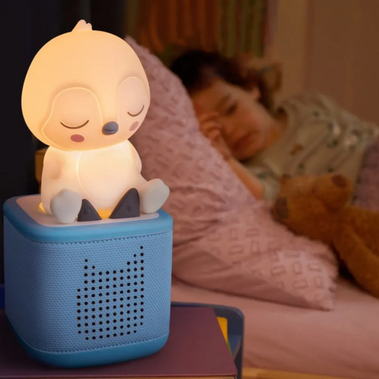 Children's night light shaped like a cartoon character on a bedside table with a child sleeping in the background.