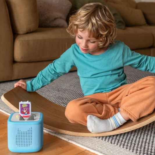 Child sitting on a wooden stool with a blue toy next to them in a living room.
