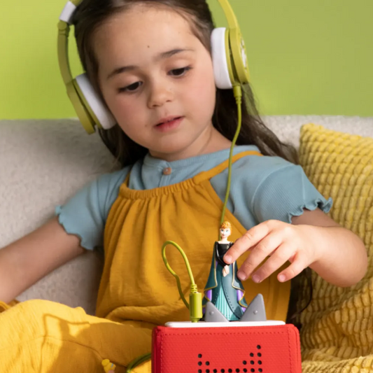 Child wearing headphones and interacting with a red device on a couch against a green wall.