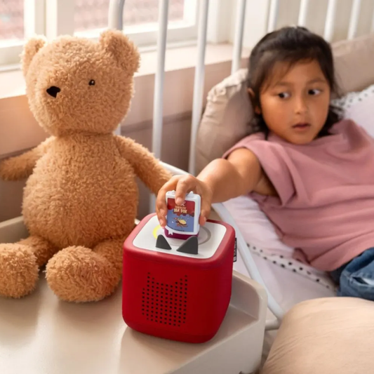 Child playing with a red toy kitchen set in a crib with a teddy bear.
