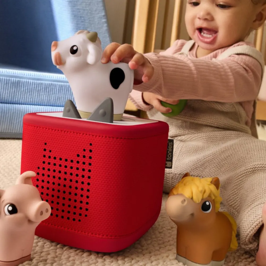 Child playing with a red toy box and animal figurines on a carpeted floor.