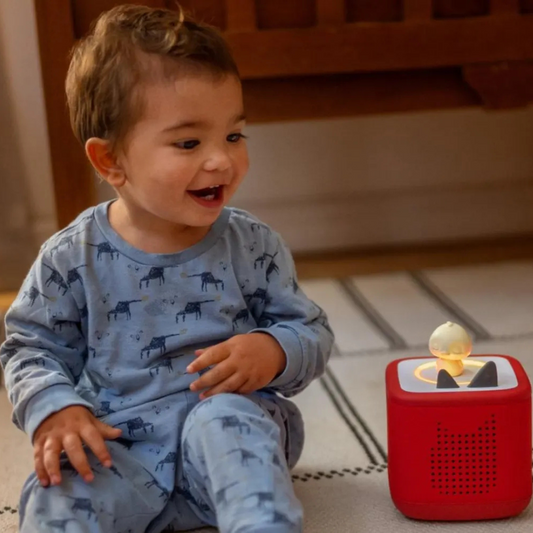 Child in blue pajamas sitting on the floor next to a red toy with a gold ball on top.