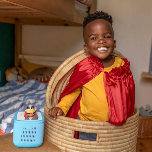 Child in a red and yellow superhero costume sitting in a woven basket with toys.