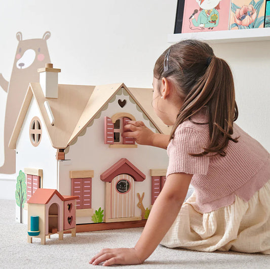 Child playing with a wooden dollhouse in a room with colorful wall art.