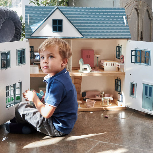 Child playing with a dollhouse in a room with furniture and decor.