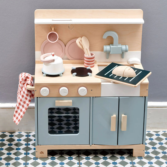 Wooden toy kitchen set with oven, stove, and utensils on a gray wall background.