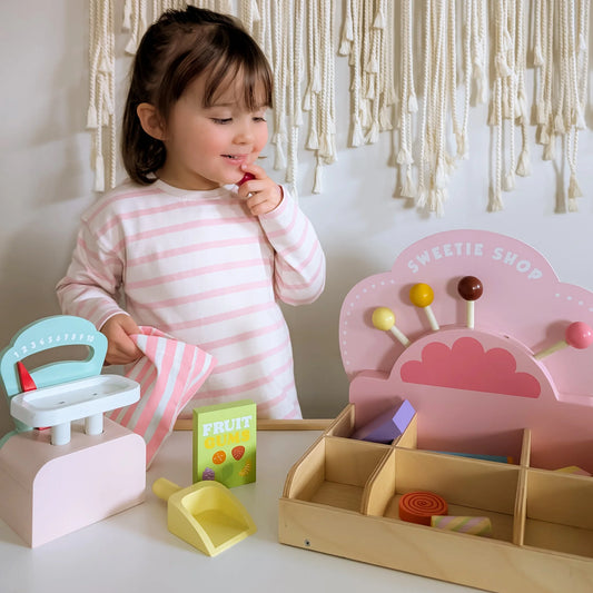 Child playing with a toy sweet shop set in a room with decorative macramé wall.