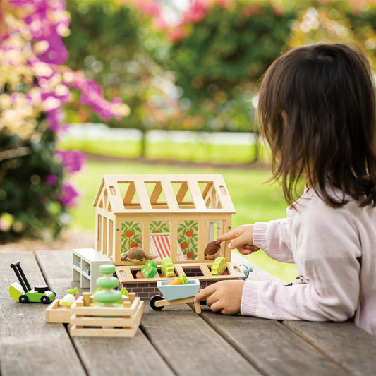 Child playing with a toy house on a wooden table outdoors
