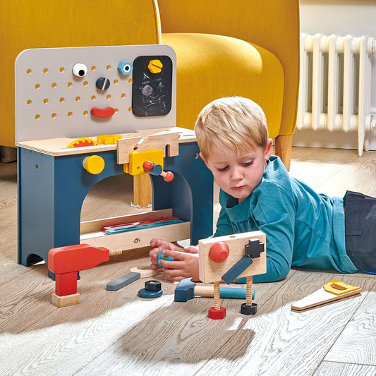 Child playing with a wooden toy workshop set on a wooden floor.