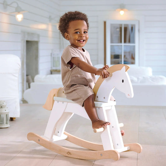 Child sitting on a wooden rocking horse in a bright, minimalistic room.