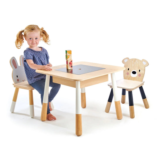 Child sitting at a wooden table with animal-themed chairs on a white background