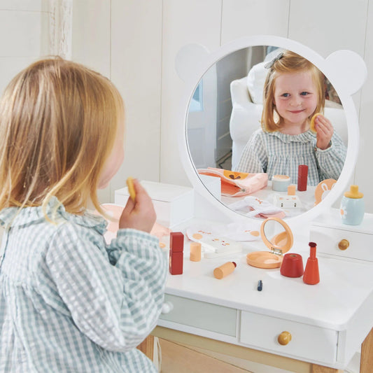 Child playing with makeup toys at a vanity table in a bright room.
