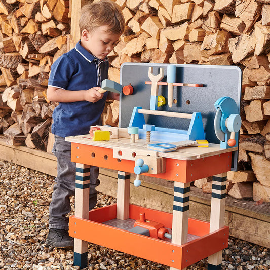 Child playing with a wooden toy workbench against a backdrop of stacked firewood.