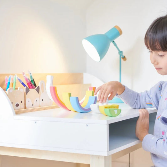 Child playing with colorful toys at a desk with a lamp in the background
