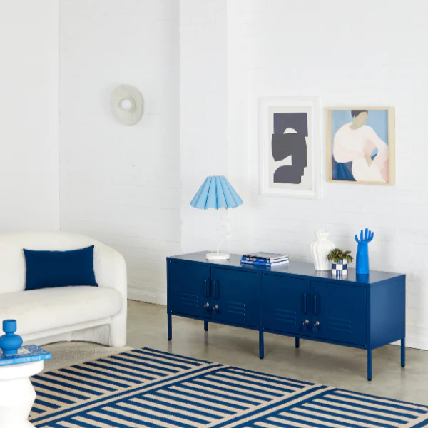 Modern living room with a blue cabinet, striped rug, and white walls.