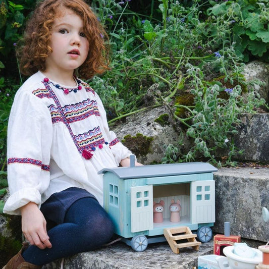 Child sitting with a toy house in a garden setting