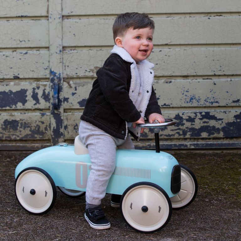 Child riding a light blue toy car against a textured wall.