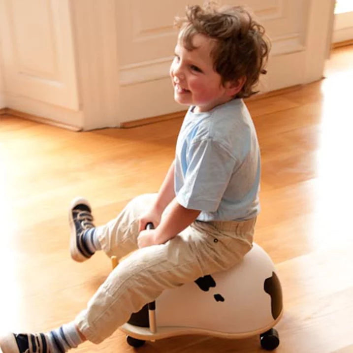 Child sitting on a white ball-shaped toy with black accents on a wooden floor.