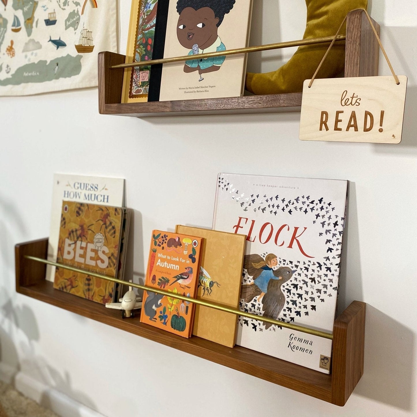Children's books on a wooden shelf with a decorative sign that says 'let's READ!' against a white wall.