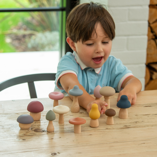 Child playing with colourful wooden mushroom with silicone tops toys on a wooden table.