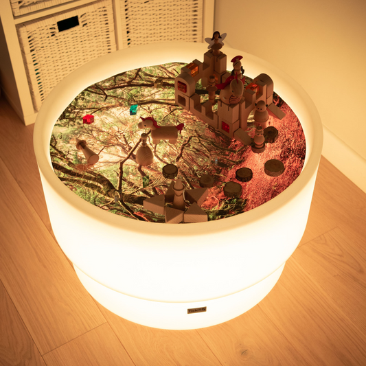 Round sensory discovery play table with a forest play scene set up on forest play mat