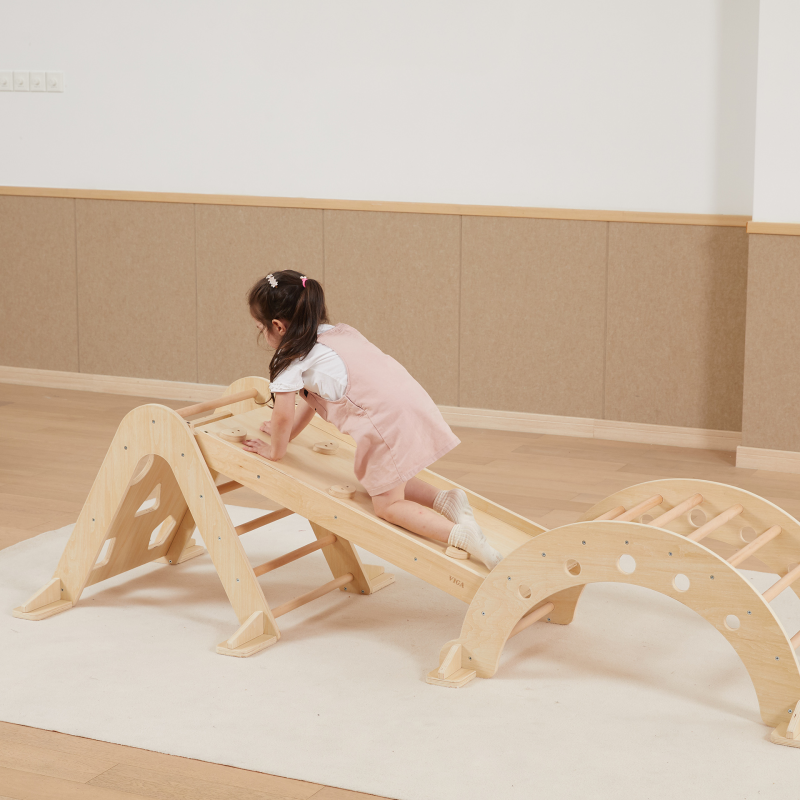 Child playing on a wooden climbing frame in a room with beige walls and flooring.