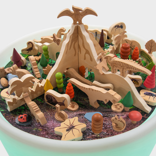 Wooden toy set with dinosaurs, trees, and a volcano on a white background