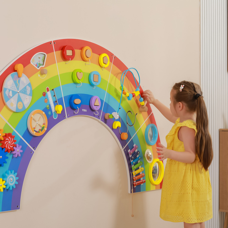 Child playing with a colourful rainbow-shaped educational toy on a wall.