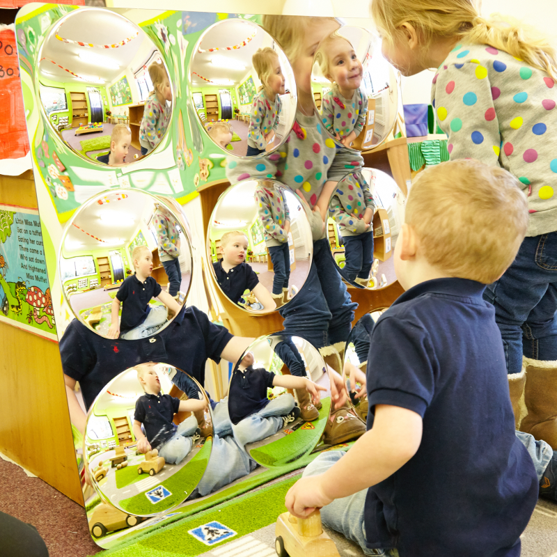 Children playing with a large mirror in a classroom setting