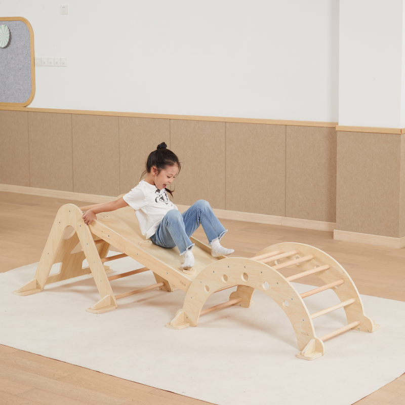 Child playing on a wooden climbing frame toy in a minimalistic room.