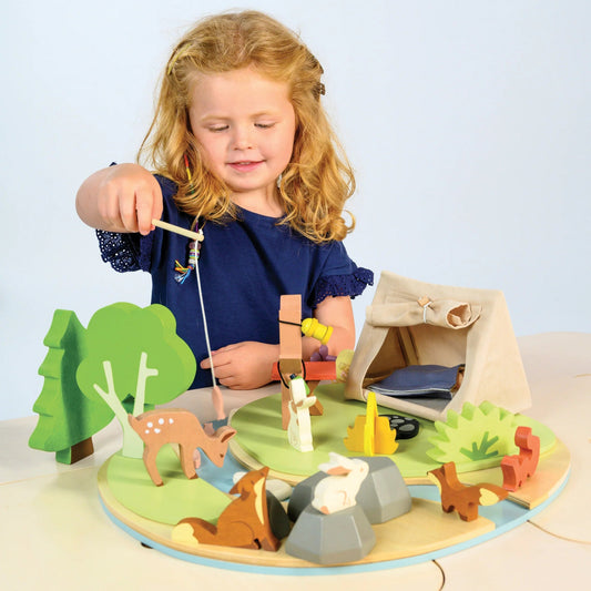 Child playing with a wooden camping playset on a light blue background