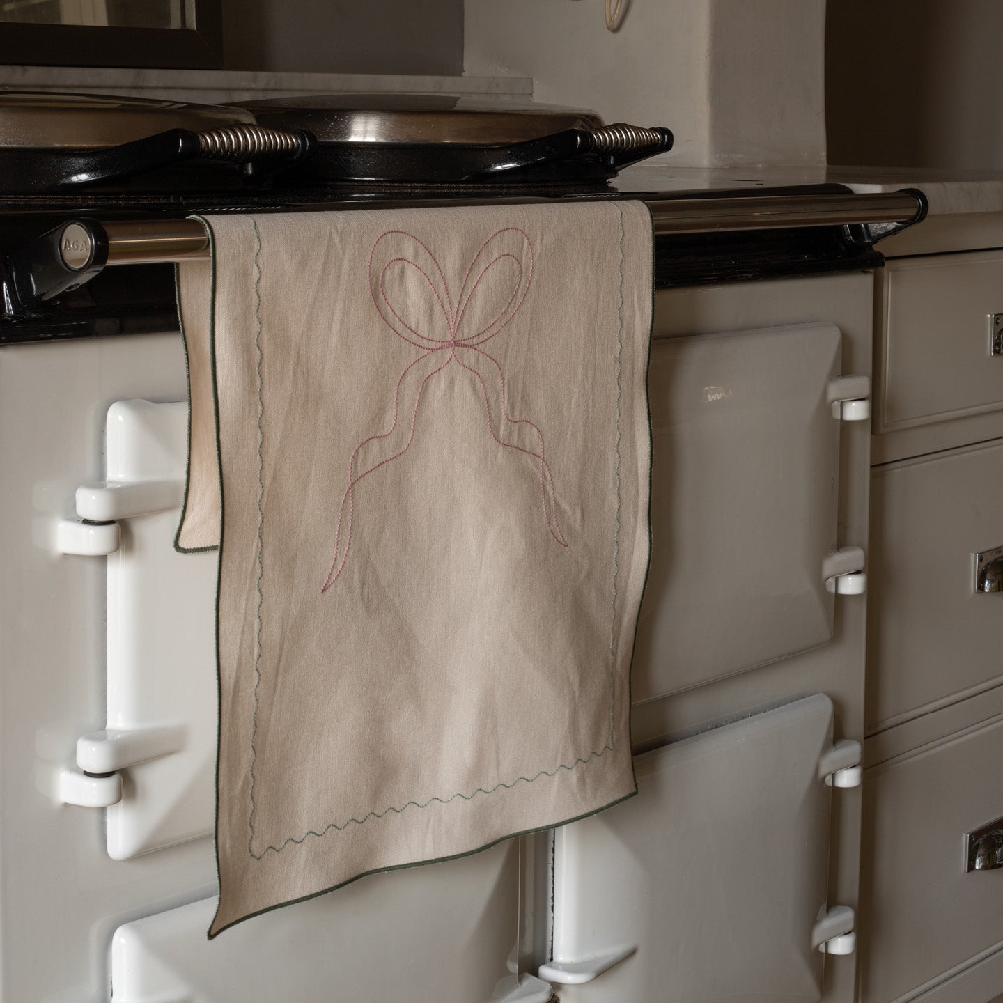Beige towel with a pink bow design hanging on a vintage-style stove.