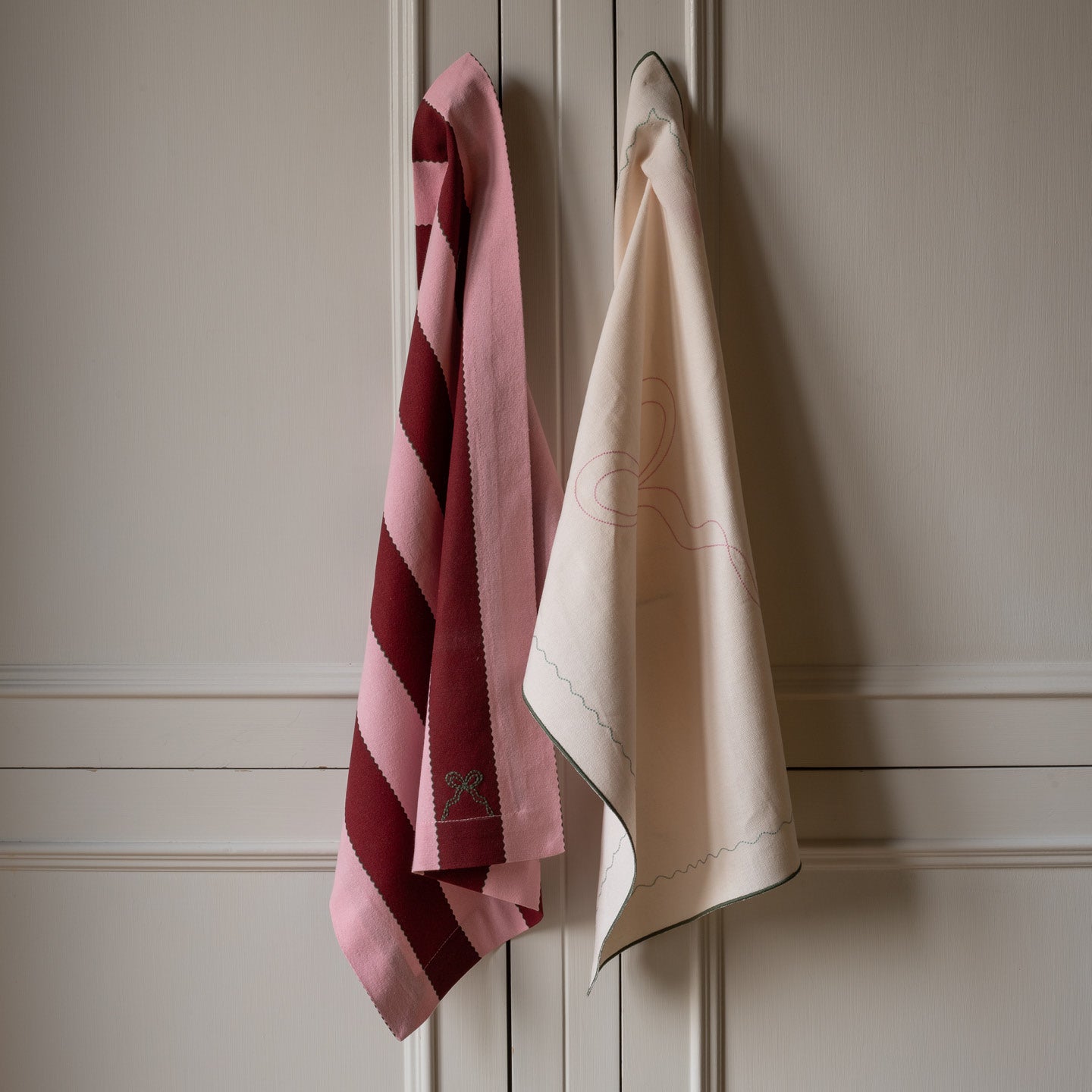 Two towels, one pink with stripes and one beige, hanging on a wooden panel.