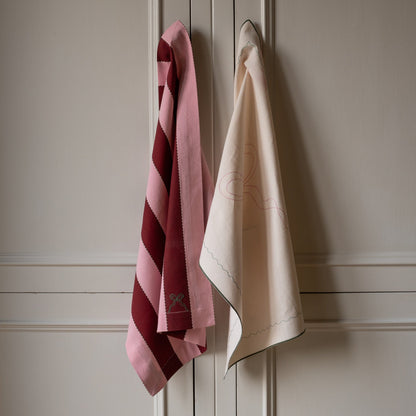 Two towels, one pink with stripes and one beige, hanging on a wooden panel.