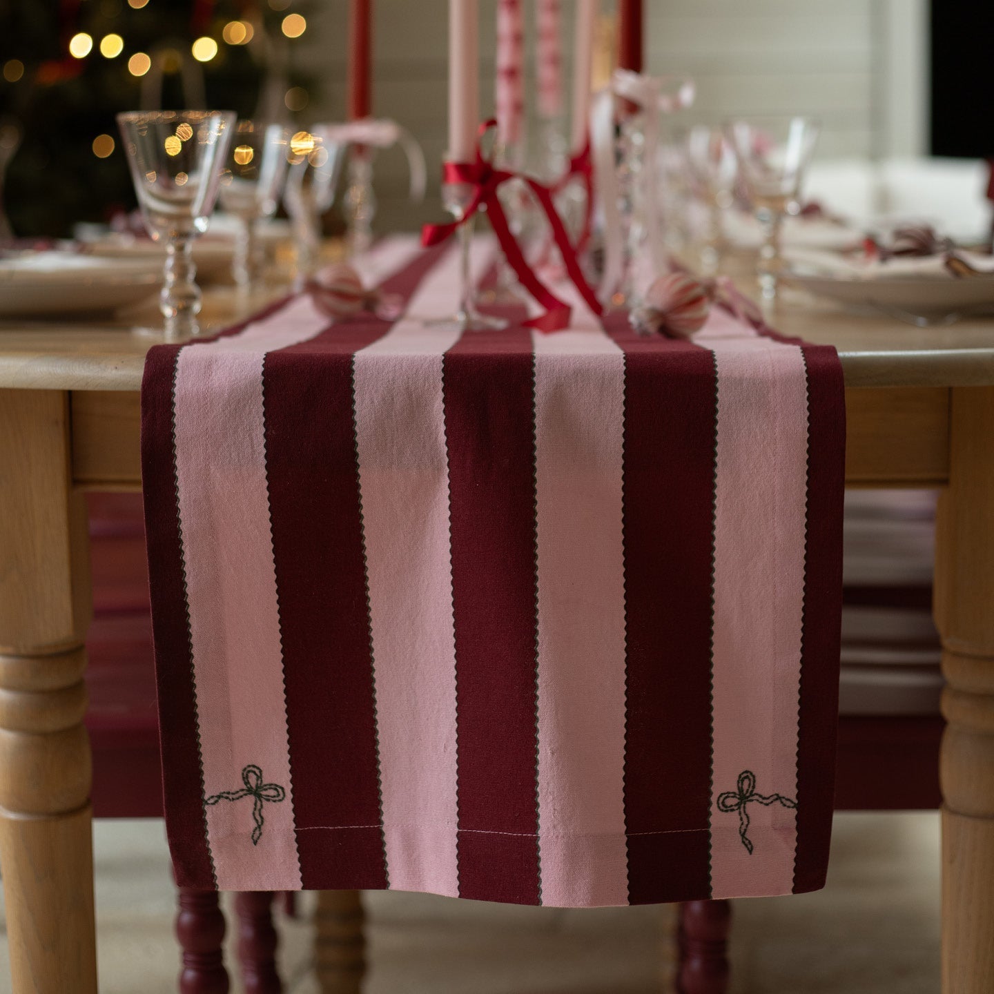 Dining table set with a striped red and white table runner, glasses, and a blurred festive background.