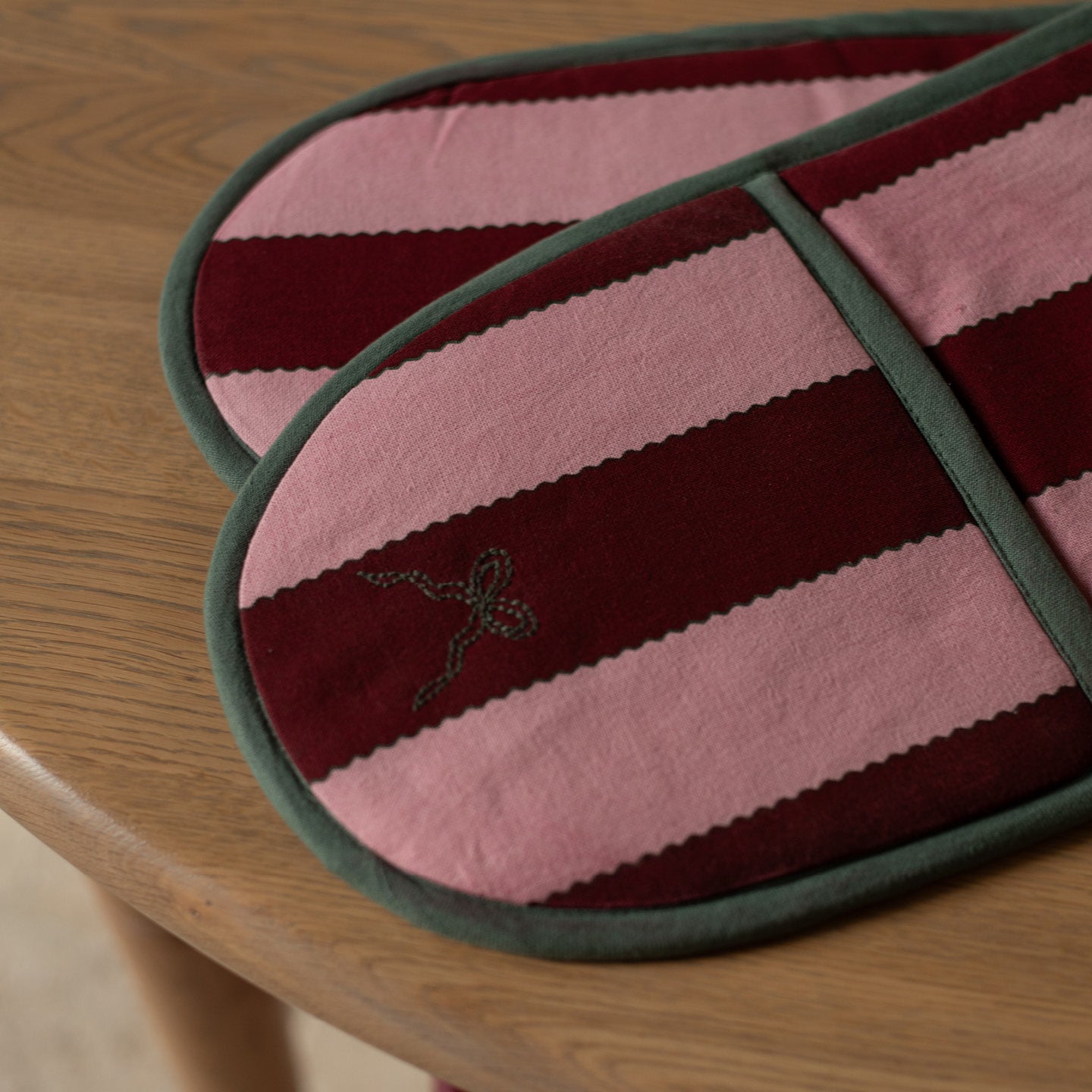 Pink and maroon striped oven mitt on a wooden surface