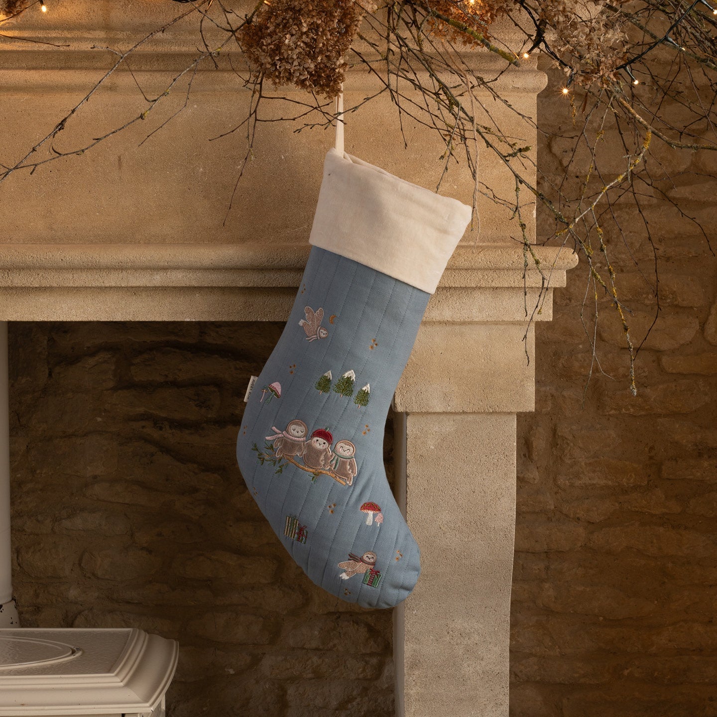 Blue Christmas stocking with embroidered designs hanging on a fireplace mantle.