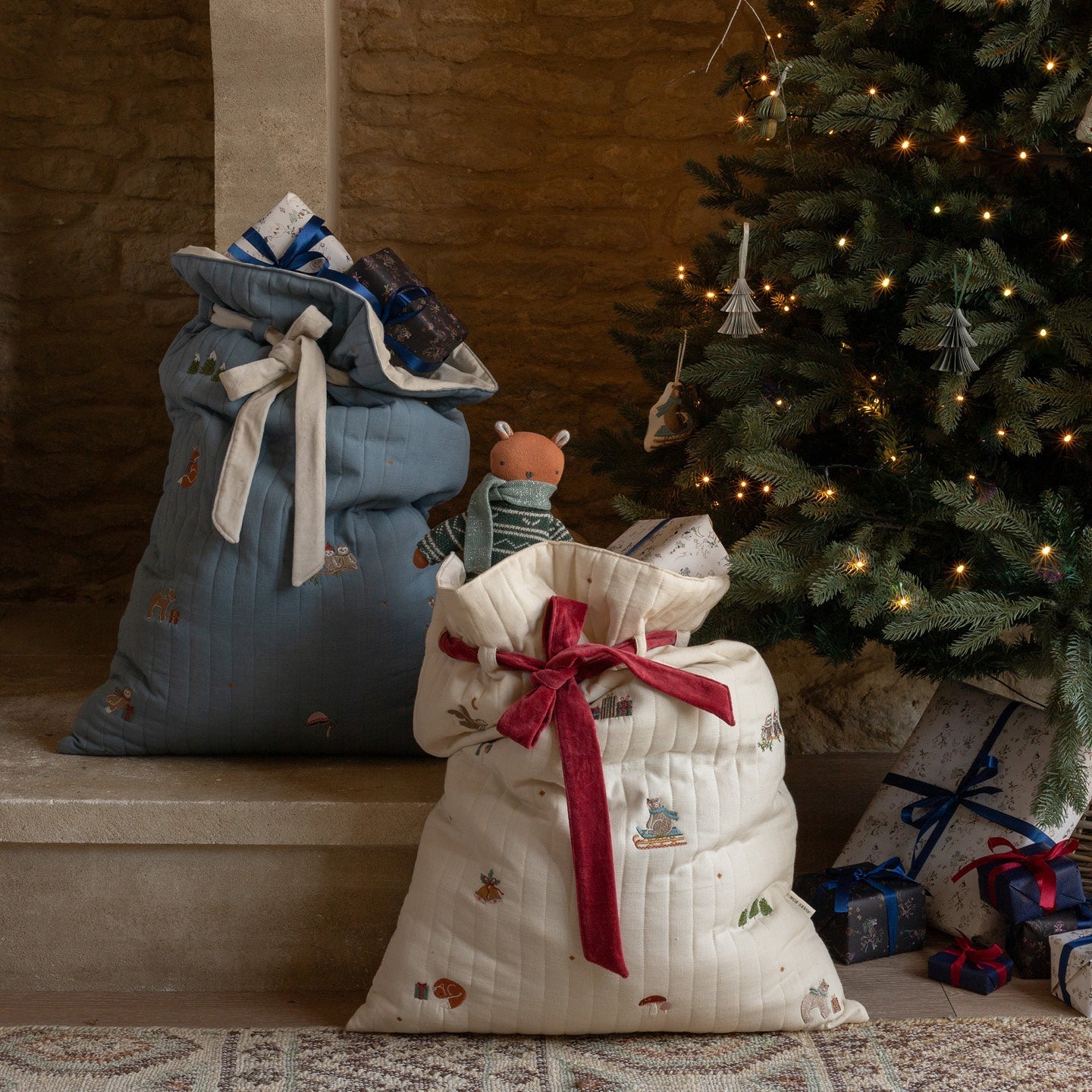 Two Christmas stockings, one blue and one white with a red bow, in front of a decorated Christmas tree.