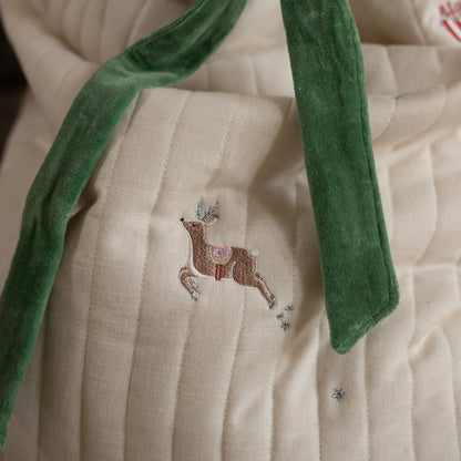 Close-up of a beige fabric with an embroidered deer design and green velvet trim.