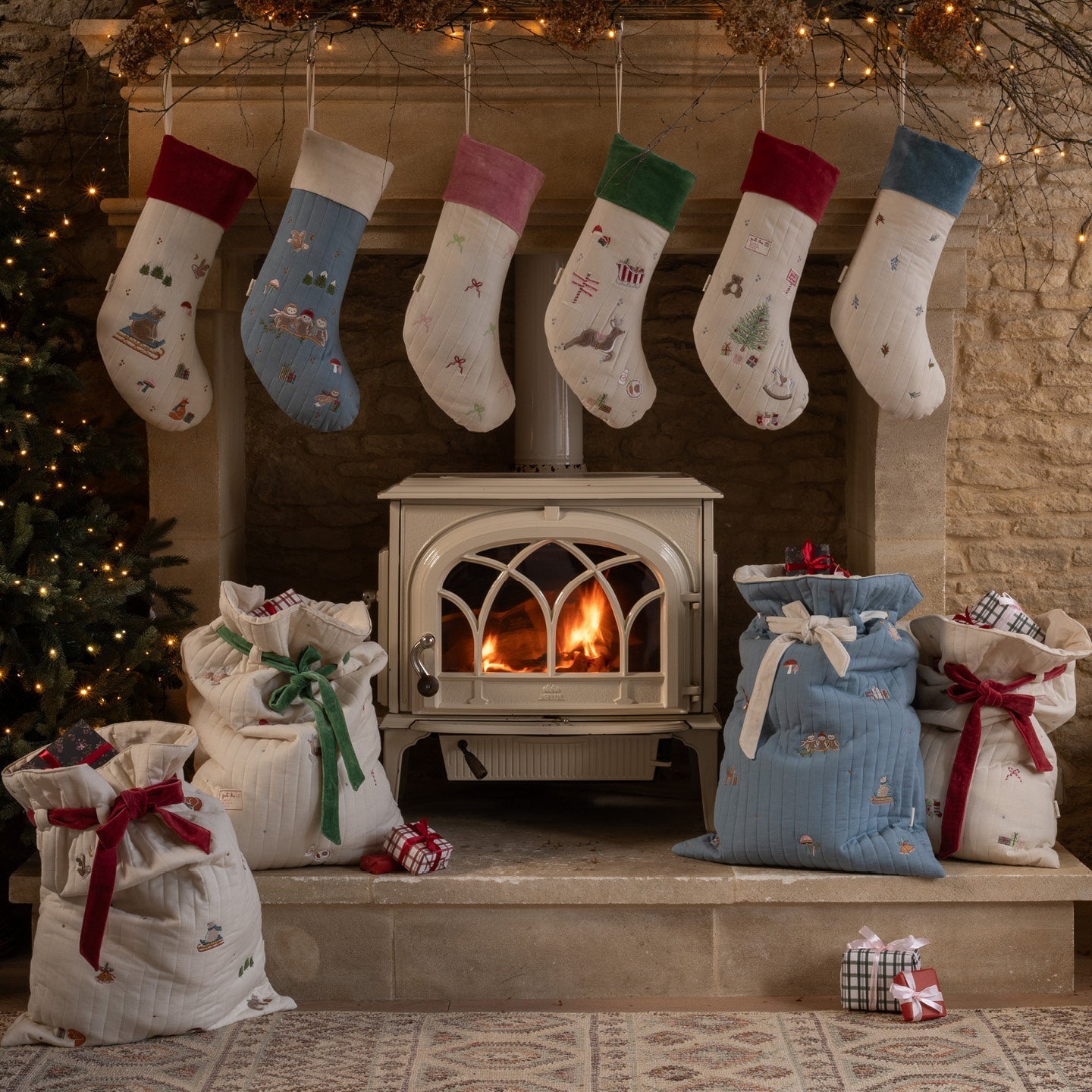 Christmas stockings and gift bags hanging above a fireplace with a warm fire.