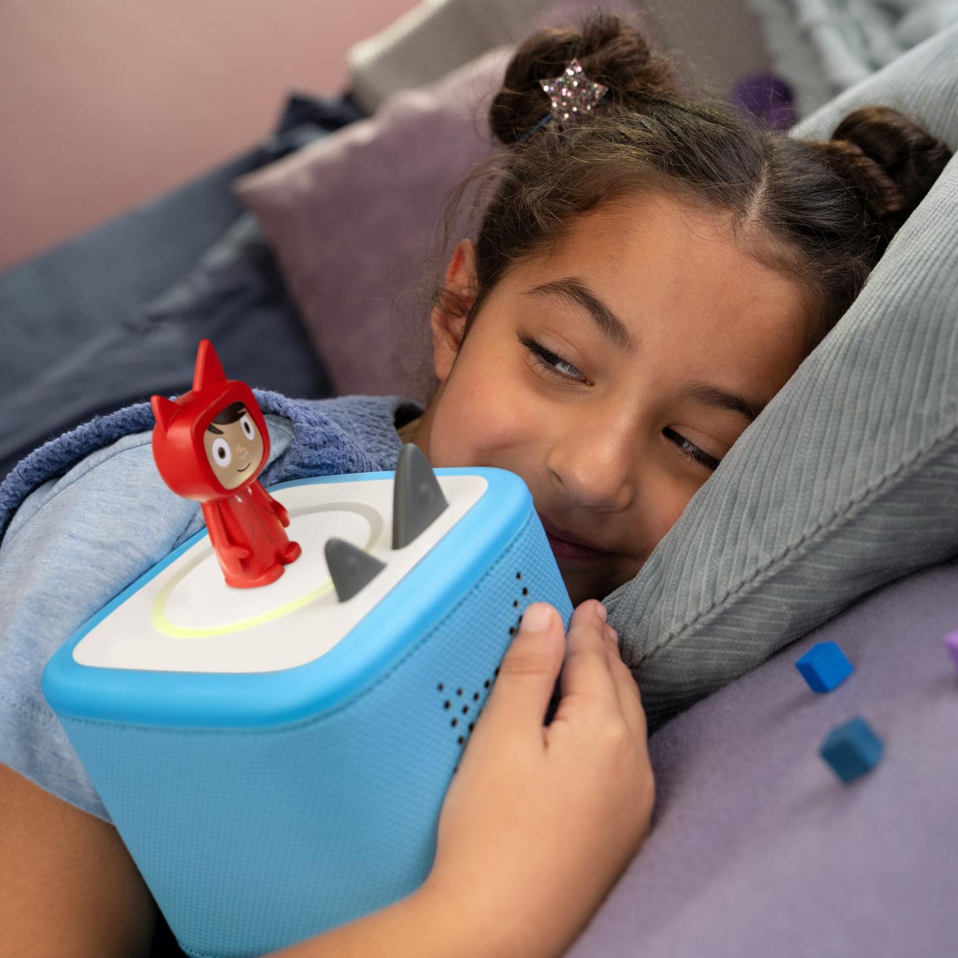 Child playing with a blue toy device featuring a red character on a bed.