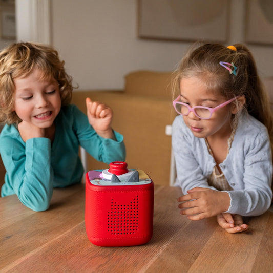 Two children playing with a red toy on a wooden table.