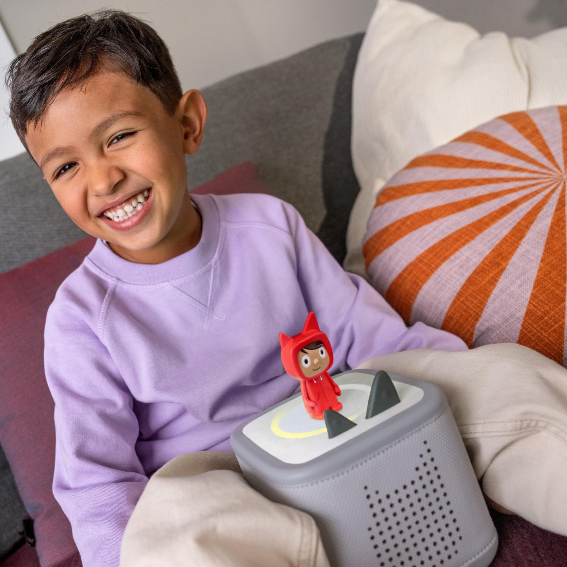Child sitting on a couch with a toy robot and a small figure on top