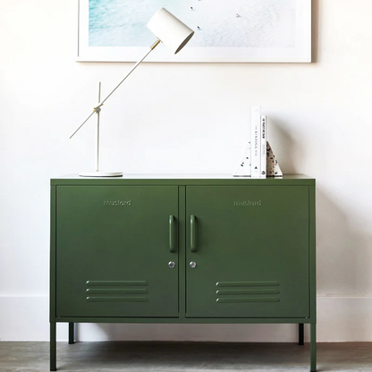 Green metal cabinet with branding, lamp, and abstract painting on a white wall.