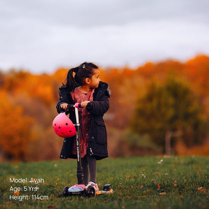 Child with a scooter and helmet in an outdoor setting with trees in the background