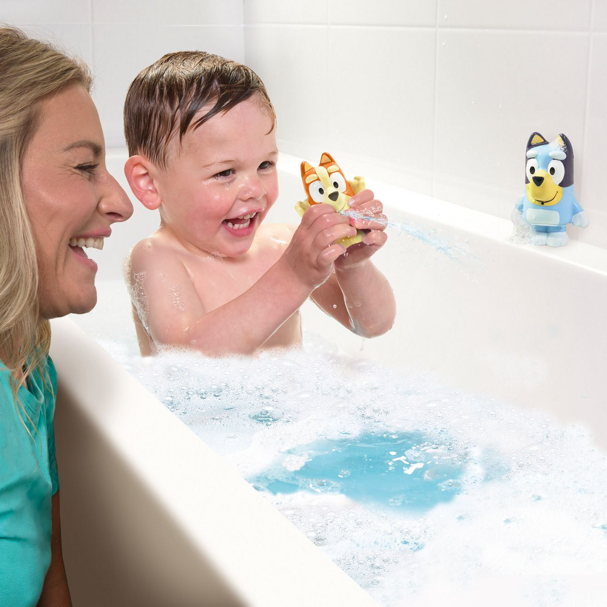 Child playing with bath toys in a bathtub with a woman watching.