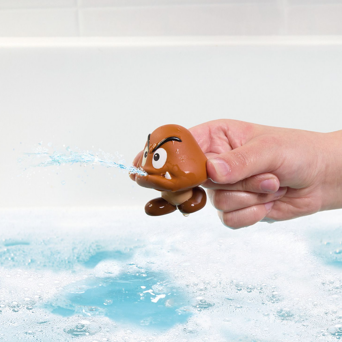 Hand holding a small brown toy with water being squirited out, against a light background.
